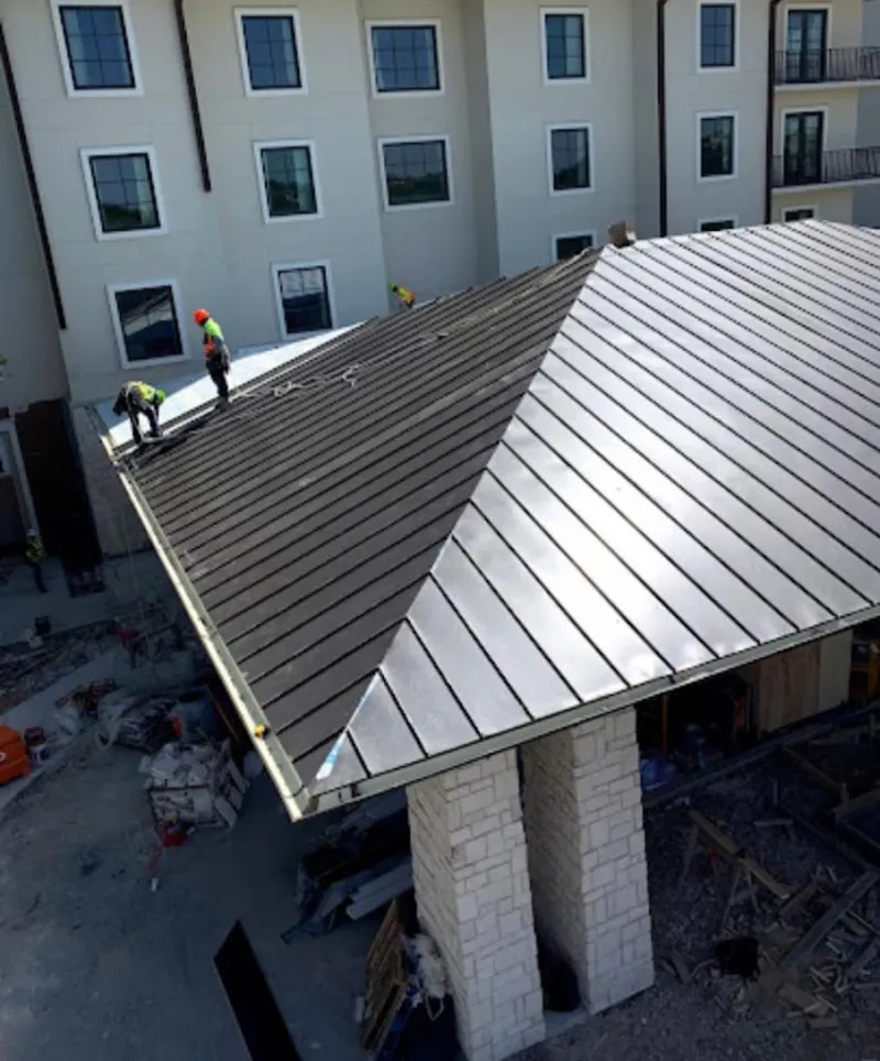 Crew installing standing seam metal roof panels on a commercial project in Indianola
